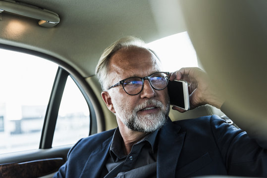 Mature businessman sitting on backseat in car, talking on the phone
