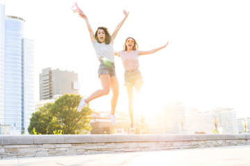 Fototapeta na wymiar Two young happy hipster girls having fun, smiling, laughing, jumping, walking outdoor on the street, summer relax concept
