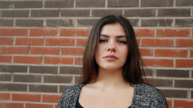 Portrait of a young confident woman against a brick wall. Slow motion shot.