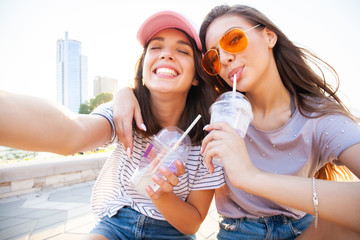 Two smiling young girls having fun while sitting on a skateboard and taking a selfie at the park.