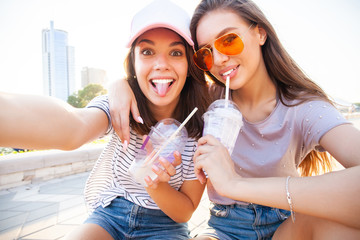 Two smiling young girls having fun while sitting on a skateboard and taking a selfie at the park.