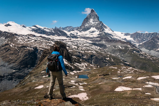 Female traveler with backpack hiking mountain trail and admiring views of Majestic Matterhorn mountain in Valais (Pennine) Alps, Switzerland.