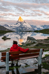 Morning shot of the golden Matterhorn (Monte Cervino, Mont Cervin) pyramid and  blue Stellisee lake. Female tourist enjoying view of early morning Matterhorn mountain is Valais Alps, Switzerland.