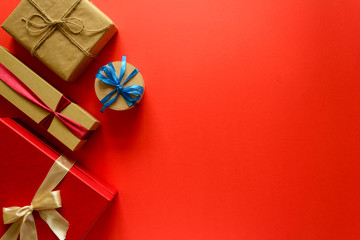 Top view on Christmas gifts wrapped in gift paper decorated with ribbon on red paper background....