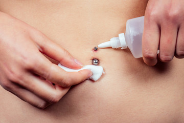 close-up hand holds cotton wool and disinfected antiseptic a drop on navel piercing. care and...