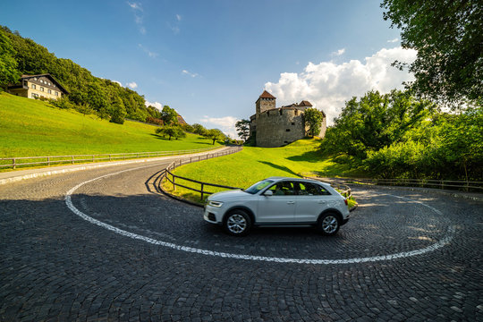 Vaduz Castle with mountain road in Liechtenstein. White car on a curvy mountain road. Alps landscape background.
