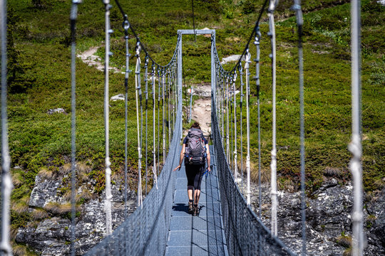 Female hiker walking on the hanging bridge over the valley on a mountain trail around Valais Swiss Alps. Hiking in a Switzerland Alps.