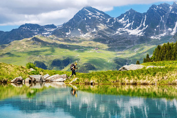 Female traveler with backpack hiking mountain trail next to a mountain lake and admiring views of...