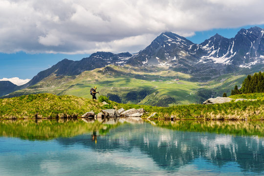 Female traveler with backpack hiking mountain trail next to a mountain lake and admiring views of Swiss Alps in Val de Bagnes area, Switzerland.