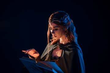Side view of mystic female beatiful elf reading magical book in darkness. © serhiibobyk