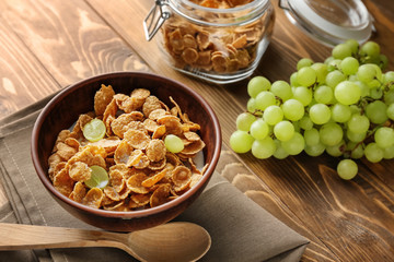 Tasty corn flakes with grape in bowl on wooden table