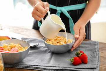 Woman pouring milk into bowl with corn flakes at table
