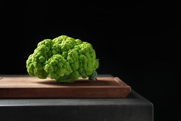 Board with green cauliflower cabbage on table against black background