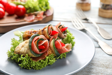 Plate with tasty zucchini rolls on light wooden table, closeup