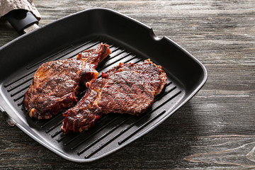 Pan with delicious grilled steaks on wooden table