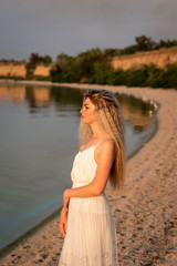 Fototapeta na wymiar Girl with magnificent hair and a white dress is standing on the beach in the evening
