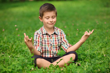 Cute little boy practicing yoga in park on summer day