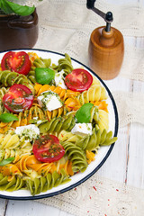 Italian food - Salad with colorful pasta, cherry tomatoes, feta cheese and fresh basil on white wooden background