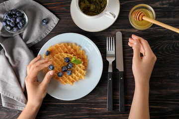 Woman eating delicious waffles with blueberries and honey on wooden background