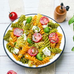 Italian food - Salad with colorful pasta, cherry tomatoes, feta cheese and fresh basil on white wooden background