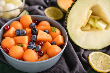 Bowl with delicious melon balls and berries on table, closeup