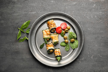 Plate with tasty zucchini rolls, green olives and tomatoes on grey table