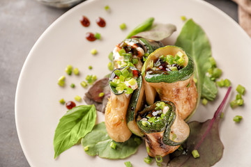 Plate with tasty zucchini rolls on light table, closeup