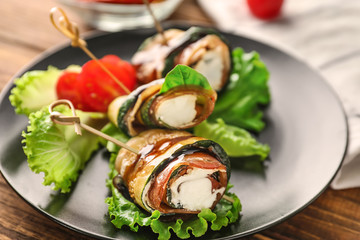 Plate with tasty zucchini rolls on wooden table, closeup