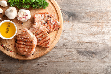 Board with delicious grilled steaks, oil and spices on wooden table