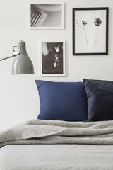 Lamp above grey blanket on bed with cushions in minimal bedroom interior with posters. Real photo