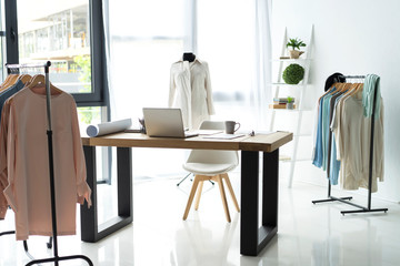 Creative fashion designer desk or workplace with sewing equipment, fabrics, templates, modern stylist inspirational office, dressmaker atelier with mannequin and clothes on hangers, couturier showroom