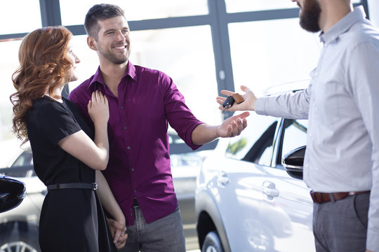 Smiling couple getting car keys from a dealer in a showroom