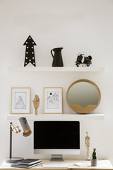 Wall shelves with decor and simple posters above wooden home office desk with metal lamp, mockup...