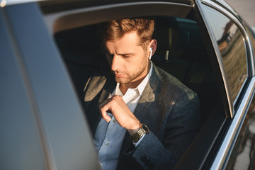 Portrait of concentrated caucasian man wearing businesslike suit and earpod, back sitting while...