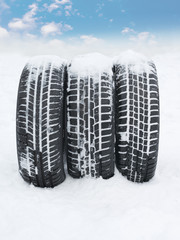 Three snowy winter tyres in front of blue sky