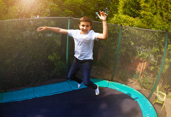 Fototapeta na wymiar Happy boy jumping high on the backyard trampoline