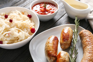 Tasty sauerkraut with grilled sausages and sauces on wooden table