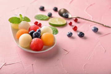 Plate with tasty melon balls and berries on color table