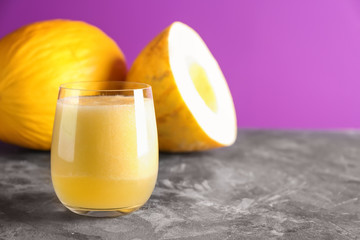Glass of fresh melon smoothie on grey table against color background
