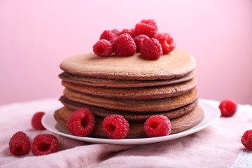 Plate with stack of tasty chocolate pancakes and raspberries on table