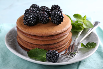 Plate with tasty chocolate pancakes and blackberries on light table