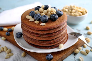 Tasty chocolate pancakes with blueberries and peanuts on plate