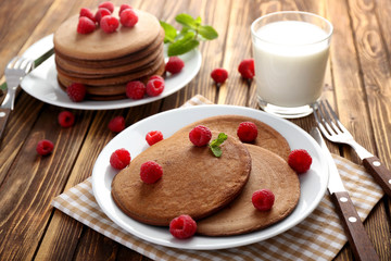 Plate with tasty chocolate pancakes and raspberries on wooden table