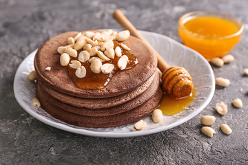 Plate with tasty chocolate pancakes, peanuts and honey on grey table