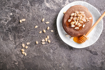 Plate with tasty chocolate pancakes, peanuts and honey on grey table