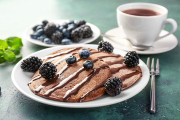 Tasty chocolate pancakes with sweet sauce and berries on plate