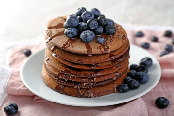 Tasty chocolate pancakes with sweet sauce and blueberries on plate
