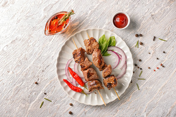 Plate with delicious shish kebab and sauce on light wooden table