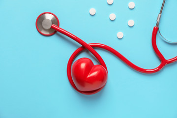 Medical stethoscope, pills and red heart on color background. Cardiology concept