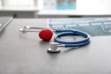 Medical stethoscope and red heart on grey table. Cardiology concept